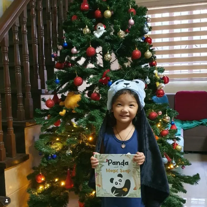 A girl in a panda hat holding the book by a Christmas tree