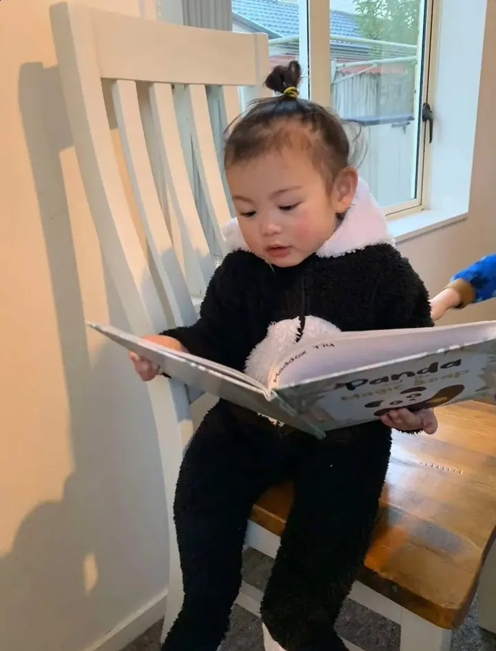 A toddler in a panda onesie reading the book